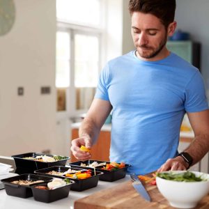 young fit man preparing healthy meal prep in his kitchen as part of a comprehensive Alternative Medicine Program